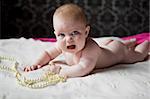 cute little girl infant lying on a white rug, along with pearl beads and invitingly crying