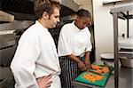 Chef Instructing Trainee In Restaurant Kitchen