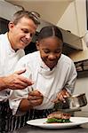 Chef Instructing Trainee In Restaurant Kitchen