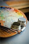Wooden artist's oil color palette with three artists paint brushes and metal twin dippers close-up on background of  art studio interior.