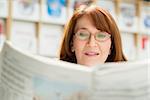 Portrait of middle aged woman with eyeglasses reading paper in library