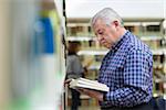 Portrait of senior retired man choosing book in library from shelf. Copy space
