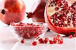 Ripe pomegranates and glass bowl of seeds on white background