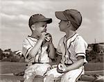 ANNÉES 1960 LITTLE LEAGUE BASEBALL BOYS EN UNIFORMES MANGER DES HOT-DOGS ET DES CASQUETTES