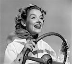 FEMME SOURIANTE DES ANNÉES 1950 AVEC MAINS SUR LE VOLANT AVEC LE VENT SOUFFLANT RETOUR CHEVEUX & ÉCHARPE STUDIO EN PLEIN AIR