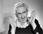 1960s ELDERLY WOMAN IN GRANNY GLASSES HOLDING HAND UP NEAR FACE WITH MOUTH OPEN LOOKING AT CAMERA