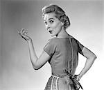 1950s HOUSEWIFE WOMAN WEARING APRON WHISTLING IN SURPRISE POINTING HAND STUDIO