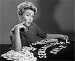 1950s 1960s PORTRAIT BLONDE WOMAN LOOKING AT CAMERA SPELLING OUT SENSATIONAL SALE WITH CUTOUT GRAPHIC DESIGN  LETTERS