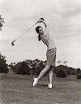 1960s WOMAN PLAYING GOLF TEEING OFF GOLF BALL FROM TEE WITH DRIVER SUMMER OUTDOOR