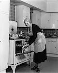 1940s ELDERLY WOMAN TAKING PAN OF ROLLS OUT OF OVEN LOOKING AT CAMERA
