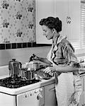 1950s HOUSEWIFE IN APRON STIRRING FOOD IN SAUCEPAN ON STOVE