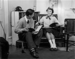 1950s TEEN BOY & GIRL SITTING IN LIVING ROOM DRINKING SODA & LISTENING TO RECORDS