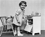 1940s 1950s SMILING LITTLE GIRL TAKING TOY POT OUT OF OVEN IN MINIATURE TOY COOKING STOVE