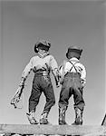 1950s BACK VIEW OF TWO BOYS DRESSED IN COWBOY COSTUME