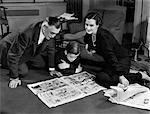 1930s 1940s FATHER AND MOTHER READING SUNDAY NEWSPAPER COMICS WITH SON SITTING ON LIVING ROOM FLOOR TOGETHER