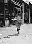 1930s NEWSPAPER BOY IN KNICKERS WALKING TOWARDS CAMERA ON STREET HOLDING PHILADELPHIA INQUIRER