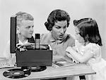 1950s MOTHER DAUGHTER & SON LISTENING TO 45'S ON PORTABLE RECORD PLAYER