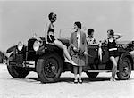 1920s 1930s FOUR WOMEN AROUND CONVERTIBLE TOURING CAR AT SEASHORE TWO IN BATHING SUITS & TWO DRESSED FOR FASHION OUTDOOR