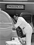 1950s SIDE VIEW OF AMBULANCE DRIVER IN WHITE UNIFORM WITH STETHOSCOPE IN POCKET OPENING BACK OF AMBULANCE TO TAKE PATIENT OUT