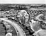 1960s FAMILY PORTRAIT IN MAGNIFYING GLASS SUPERIMPOSED OVER SUBURBAN HOUSING DEVELOPMENT