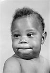 1960ER JAHRE PORTRÄT DES AFROAMERIKANISCHEN BABY MACHEN EIN LUSTIGES GESICHT, SEINE LIPPEN BEIßEN