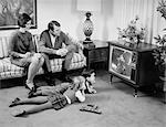 1960s FAMILY OF 4 WATCHING TELEVISION IN LIVING ROOM PARENTS ON COUCH KIDS LYING ON FLOOR