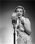 1950s PORTRAIT WOMAN ENTERTAINER SINGING INTO A MICROPHONE STUDIO LOOKING AT CAMERA