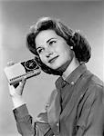 1960s PORTRAIT OF SMILING TEENAGE GIRL TILTING HEAD TO LISTEN TO PORTABLE RADIO HELD IN HAND TO EAR