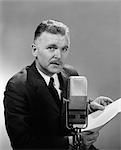 ANNÉES 1950 MAN READING AT MICROPHONE RADIO BROADCAST LOOKING AT CAMÉRA INTÉRIEURE