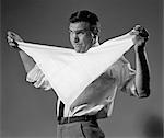 1960s MAN HOLDING CLOTH DIAPER FOLDED IN TRIANGLE UNDER CHIN WITH SAFETY PINS IN MOUTH LOOKING AT CAMERA ANGRILY