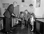 1960s FAMILY IN TV SHOWROOM TRYING SET WHILE SALESMAN WATCHES