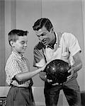 ANNÉES 1960 PÈRE FILS MONTRANT COMMENT TENIR LA BOULE DE BOWLING INTÉRIEUR