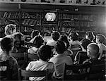 1950s BACK VIEW OF KIDS IN SCHOOL LIBRARY WATCHING TV SCREEN