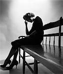 ANNÉES 1950 FEMME EN SILHOUETTE, ASSIS À L'EXTRÉMITÉ DU BANC TENANT LE FRONT DANS LA MAIN