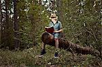 Boy sitting on tree trunk reading book