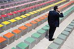 Business executive using cell phone by rows of bleachers, rear view