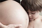 Boy resting head on mother's pregnant belly, cropped