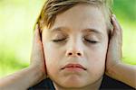 Boy covering ears with hands, eyes closed