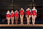 Female gymnasts of various ages standing in a row on balance beam