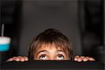 Boy peeking over top of seat during horror movie in theater