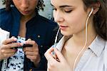 Young woman standing with friend, listening to earphones