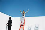 Businesswoman standing at top of ladder with arms raised in air