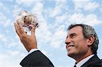 Mature man holding up transparent piggy bank filled with euros