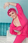 Portrait of happy young woman stretching while standing on bed