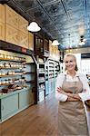 Portrait of a happy senior female spice merchant standing with arms crossed in store