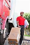 Young African American male standing with packages near delivery truck