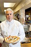 Portrait d'un milieu adulte chef tenant de pizza cuisine commerciale confiant