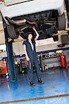 Junge weibliche Mechaniker arbeiten stehen unter angehobene Auto in der Werkstatt