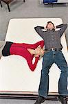 Friends lying on mattress with hands behind head in furniture store