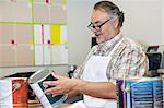 Happy mature sales clerk reading instructions paint can in hardware store